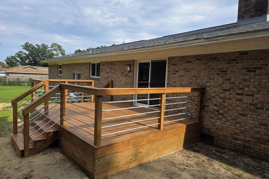 New backyard deck on a brick house with cable railing, stairs, and a skirted base