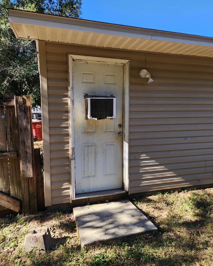 Old exterior door with a hole cut for a window unit and a rotted jamb
