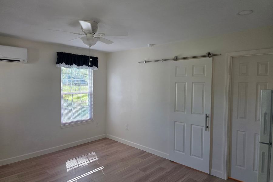 Bedroom in the new build with a sliding barn door, mini-split, and plank flooring