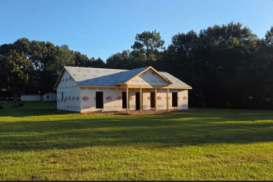 A new single-storey home under construction, dried in with house wrap and roof underlayment, the front porch roof and columns framed out