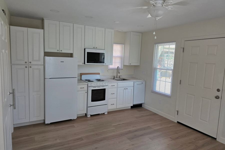 Finished kitchen inside the new build: white cabinets, plank flooring, and a new entry door