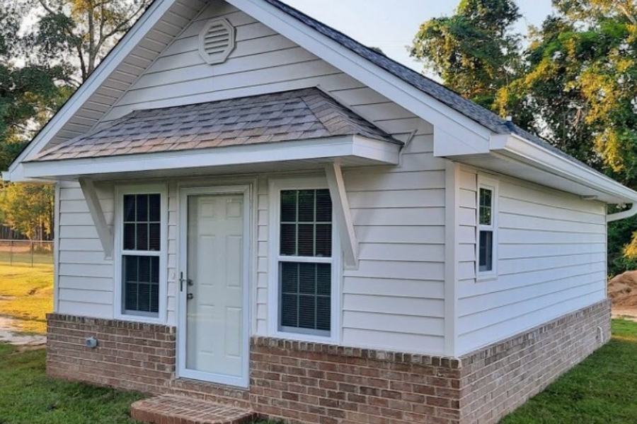 Newly built detached structure with white lap siding and a brick skirt