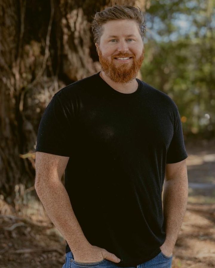 Sam Hemken, owner of Hemken Construction, standing outdoors in a black T-shirt