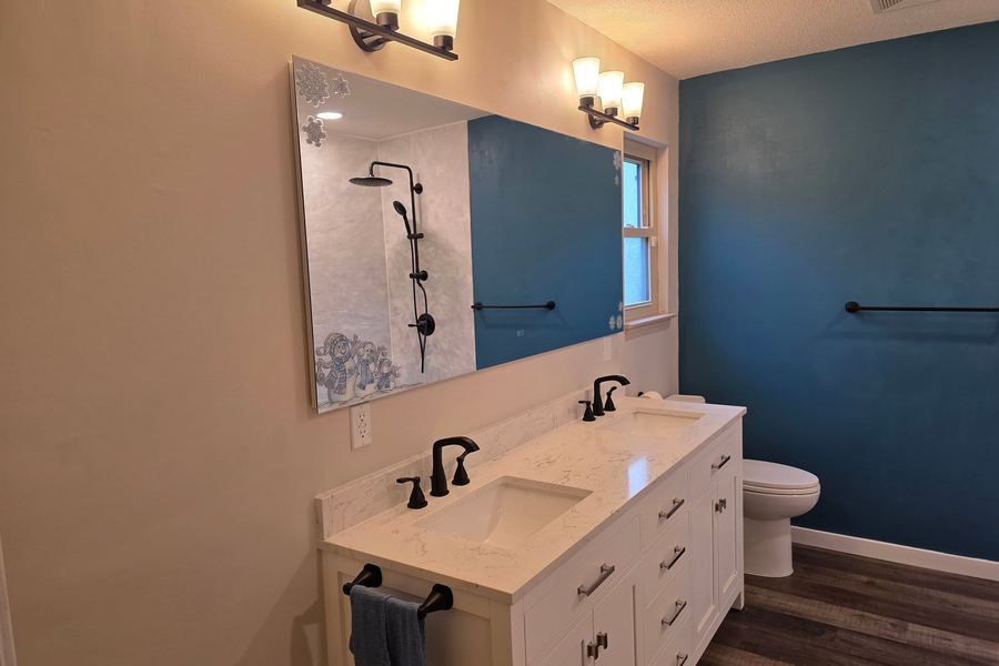 The same bathroom after: double vanity, quartz top, and a marble-look tiled shower