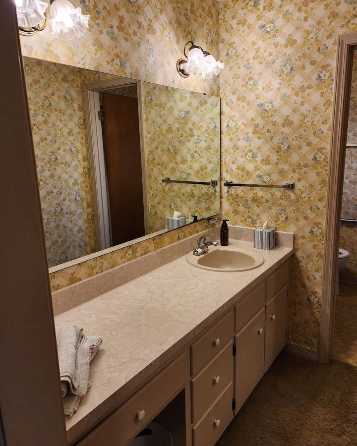 Bathroom before: floral wallpaper, laminate counter, and a single sink