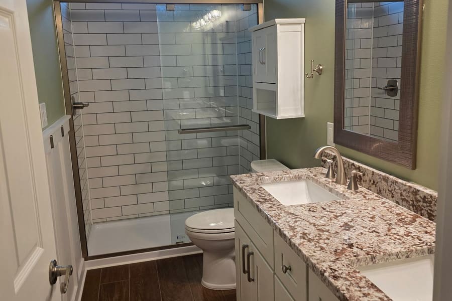 Remodeled bathroom with a subway tile walk-in shower, granite vanity top, and wood-look tile floor