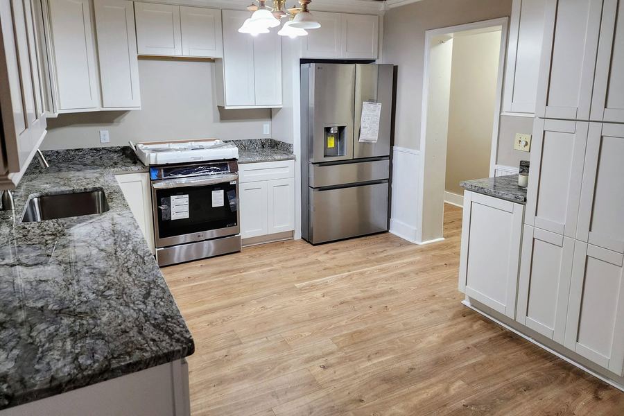 The same kitchen after: white shaker cabinets, granite counters, and new appliances