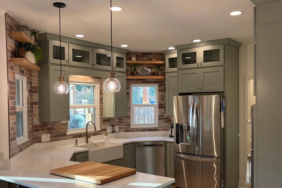 Remodeled kitchen with sage green shaker cabinets, a brick backsplash, quartz counters, and a farmhouse sink