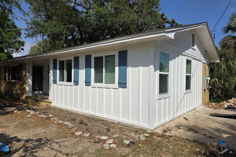 Addition finished in white board-and-batten siding with blue shutters and new windows