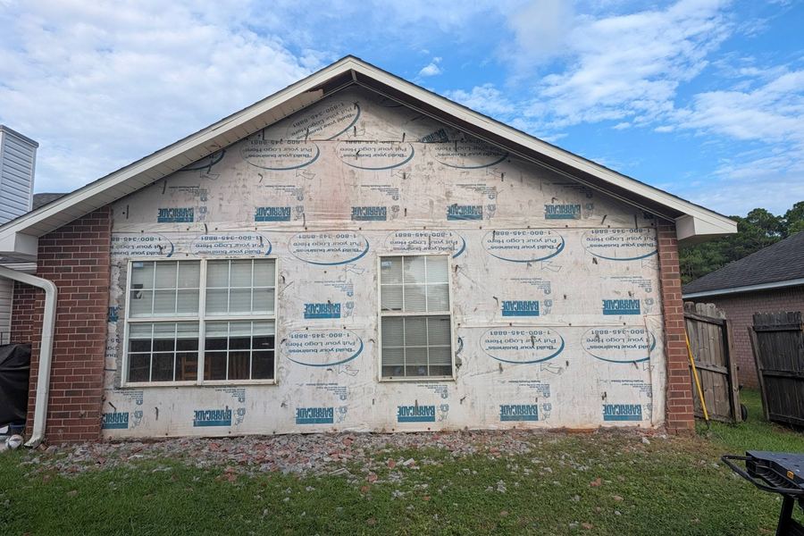 Two new windows set and flashed in a house-wrapped gable before the brick veneer goes back up